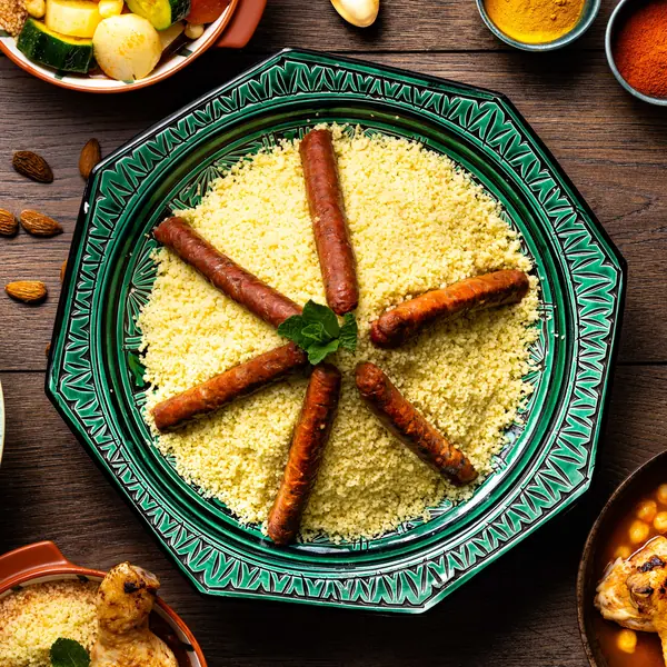 Un couscous aux merguez dans un grand plat vert en céramique