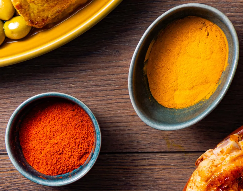 Deux bols d'épices en poudre, paprika et curcuma, sur une table en bois